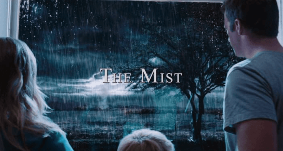 Three people looking at a poster of "The Mist" with a stormy scene.