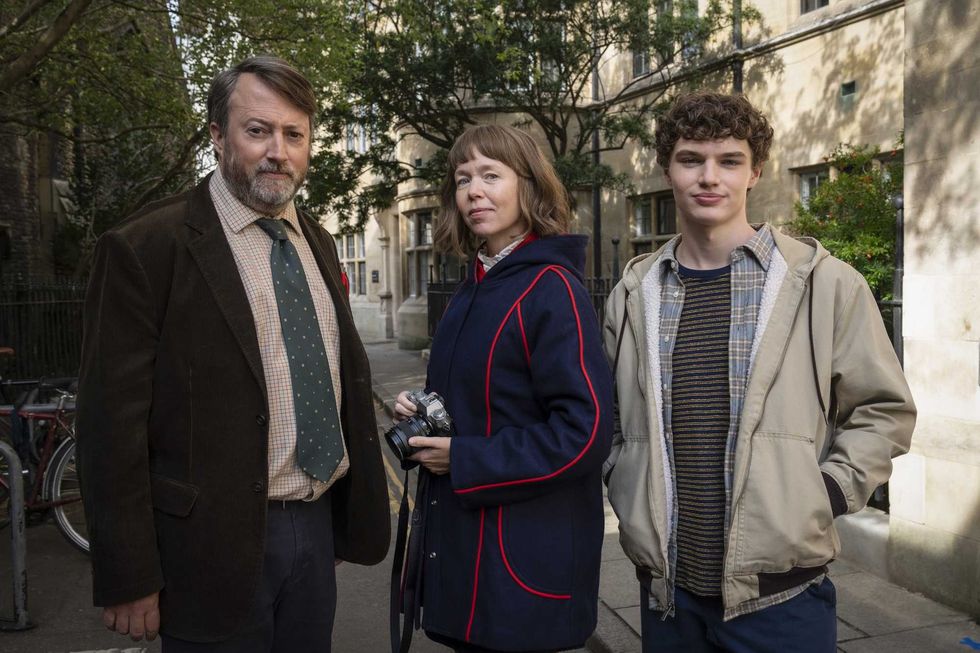 Three people outdoors, one with a camera, standing in front of a building.
