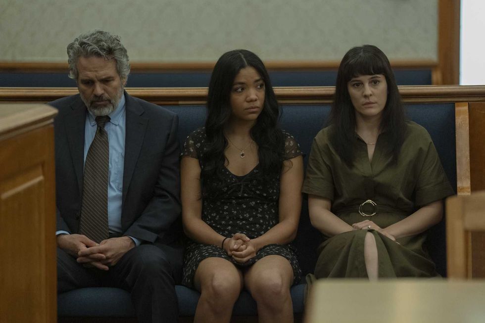 Three people sitting in a courtroom, looking serious and contemplative.