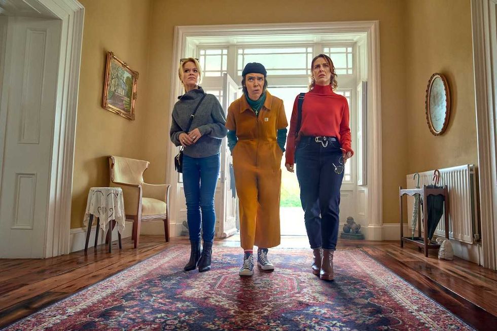 Three people walking down a hallway with a patterned rug and large window.