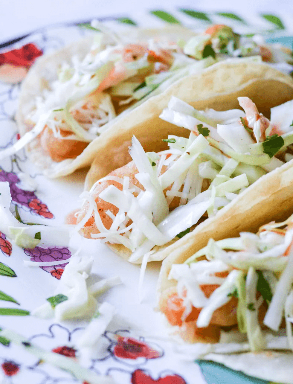 Three shrimp tacos with cabbage on a colorful, floral plate.