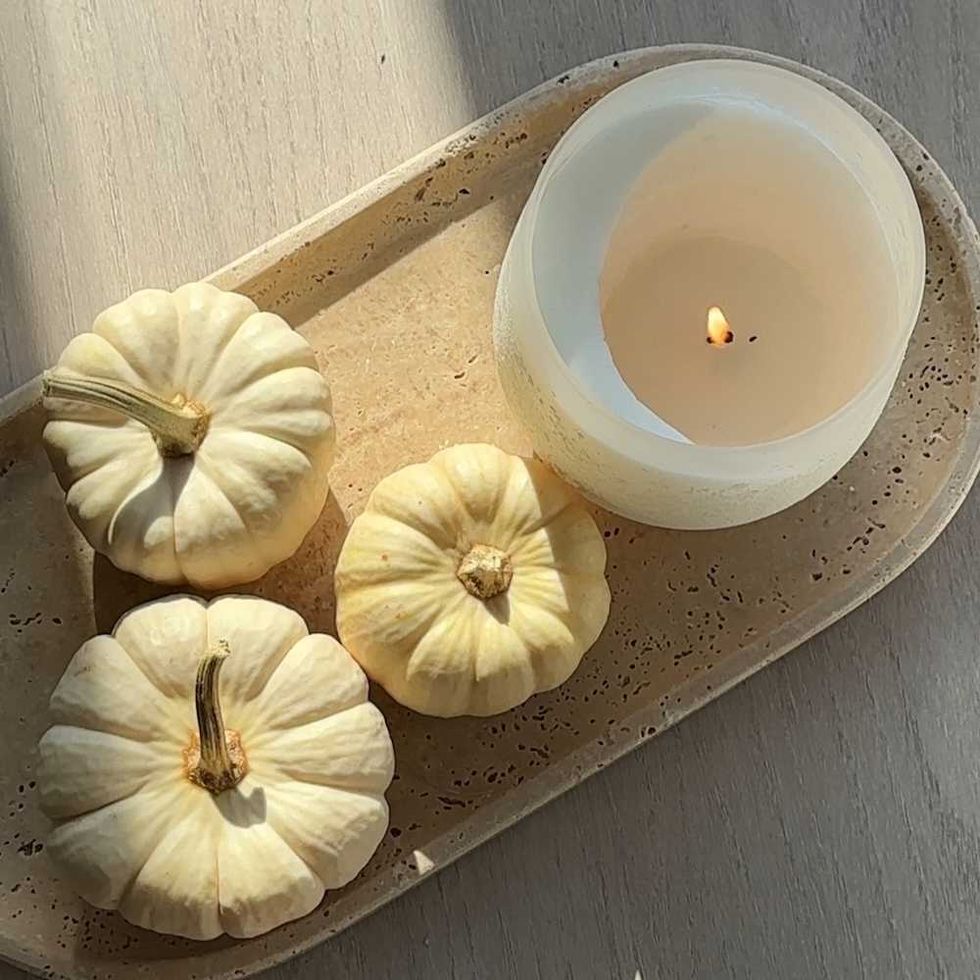 Three small white pumpkins and a lit candle on a beige tray.