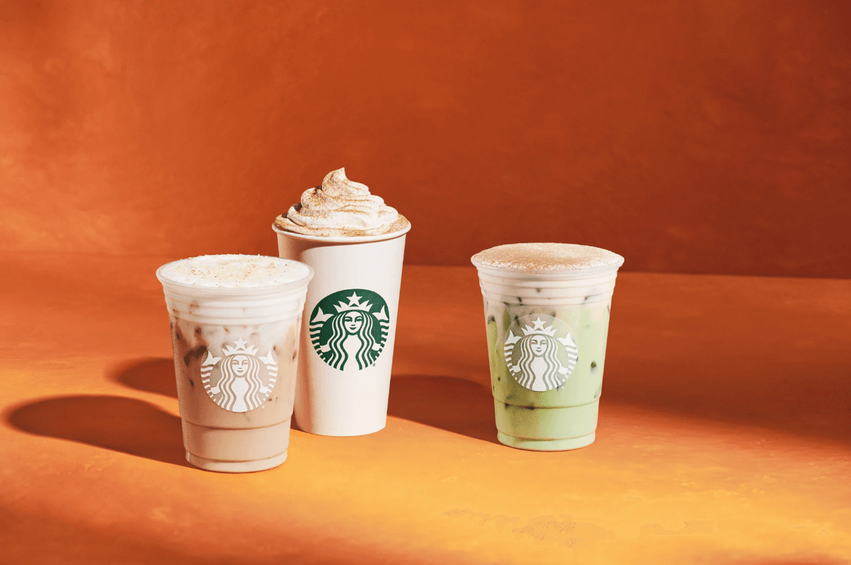Three Starbucks drinks on an orange background: two iced, one whipped cream-topped.