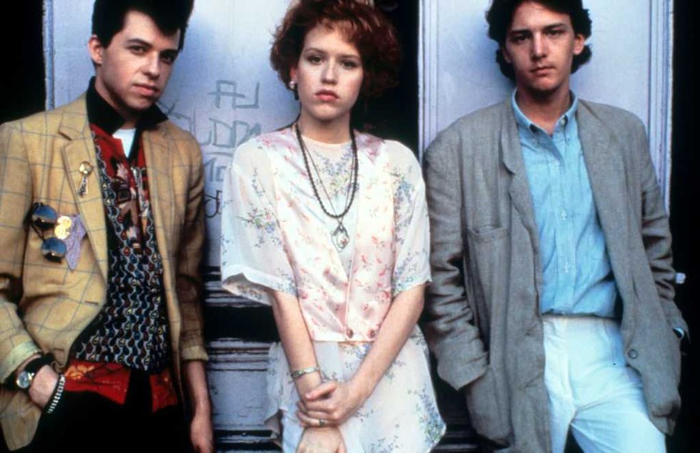 Three stylishly dressed young people stand against a wall, posing with serious expressions.