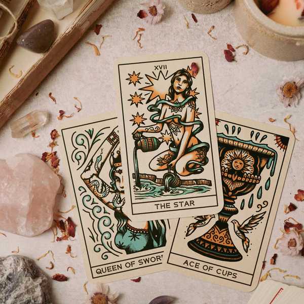 Three tarot cards: The Star, Queen of Swords, and Ace of Cups on a decorated table.