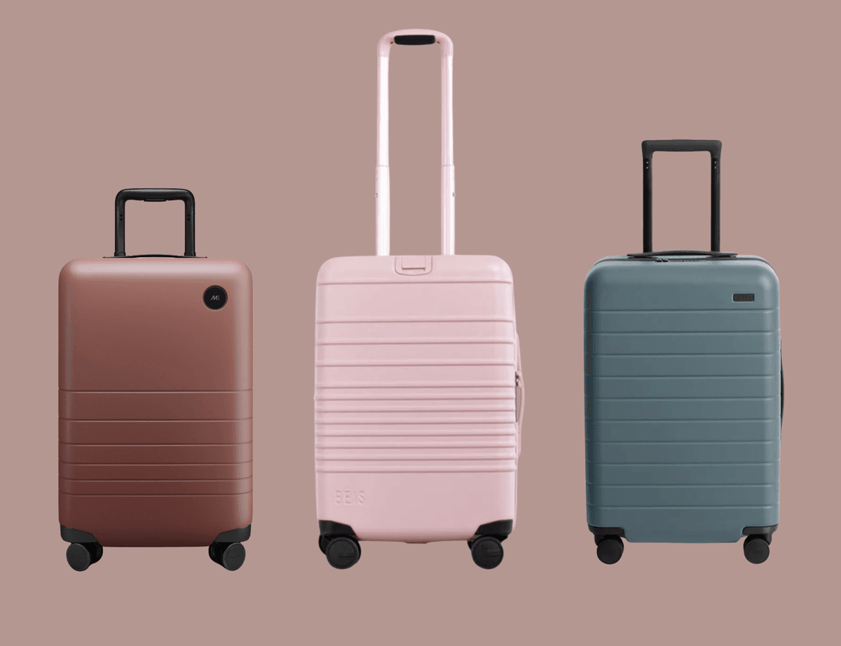 Three wheeled suitcases: brown, pink, and teal, on a solid background.