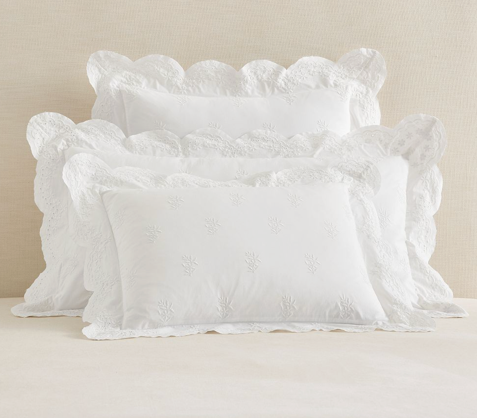 Three white pillows with embroidered lace edges stacked on a beige surface.