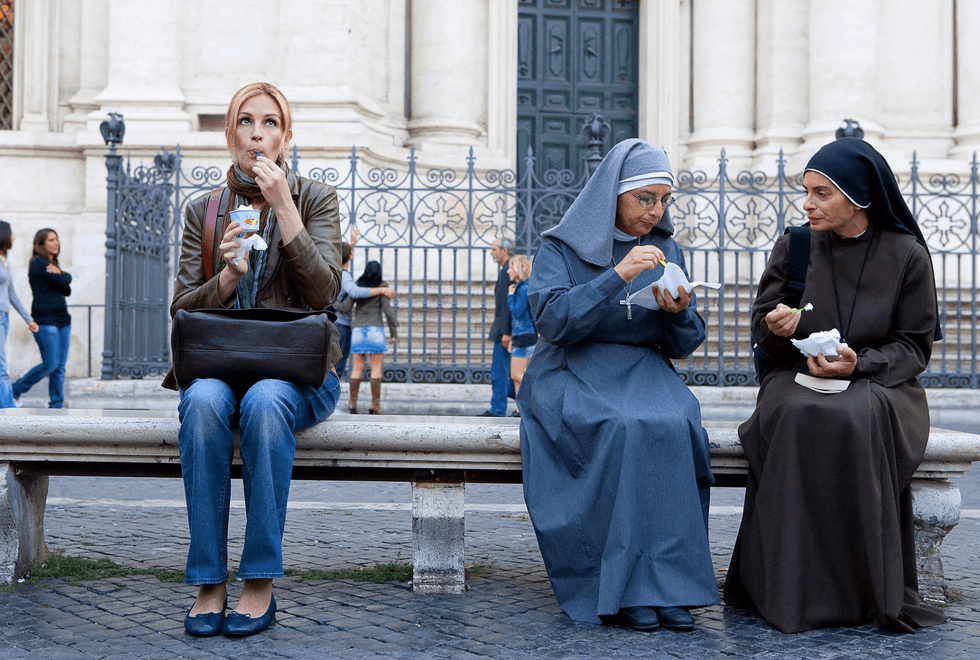 Three women on a bench enjoy ice cream; two are nuns in habits, one in casual clothing.