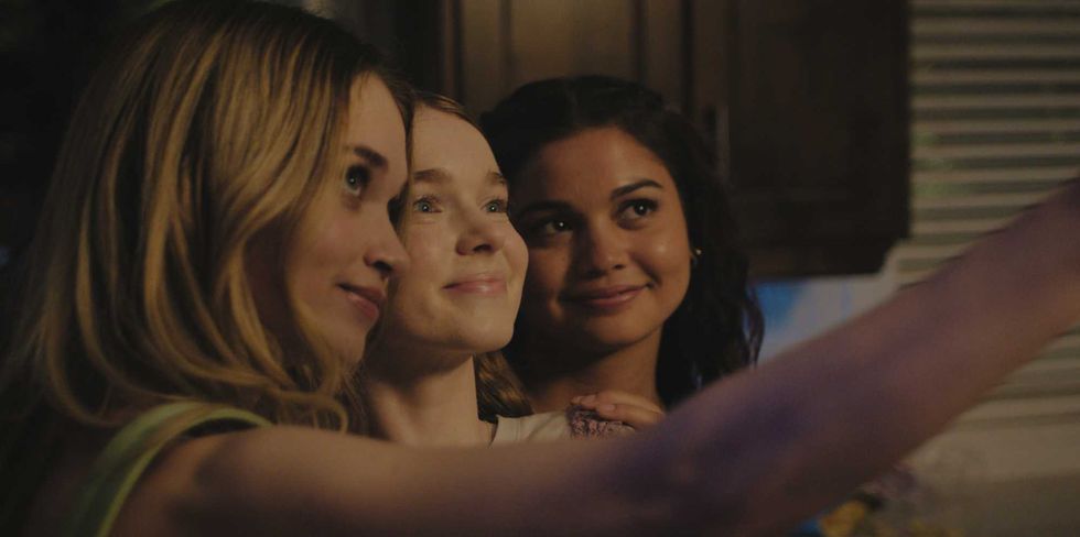 Three women smiling and taking a selfie together indoors.