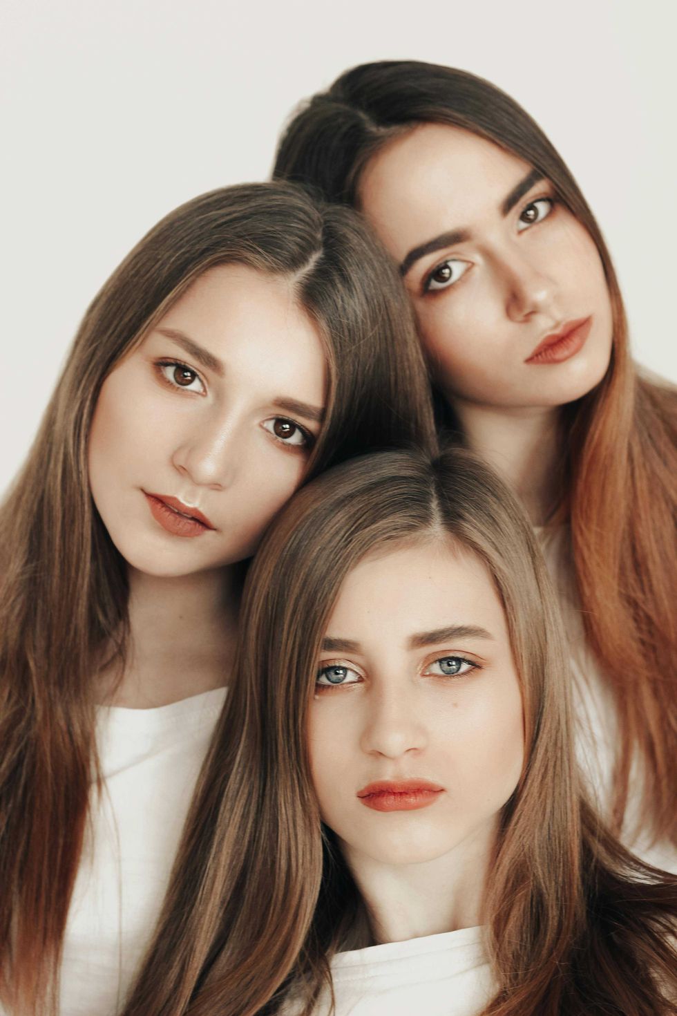 Three women with long hair and neutral expressions against a plain background.