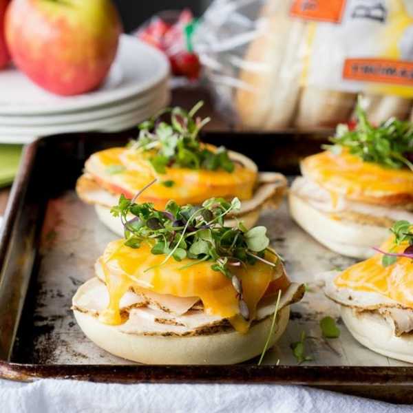 Toasted English muffins with turkey, melted cheese, and fresh greens on a tray.