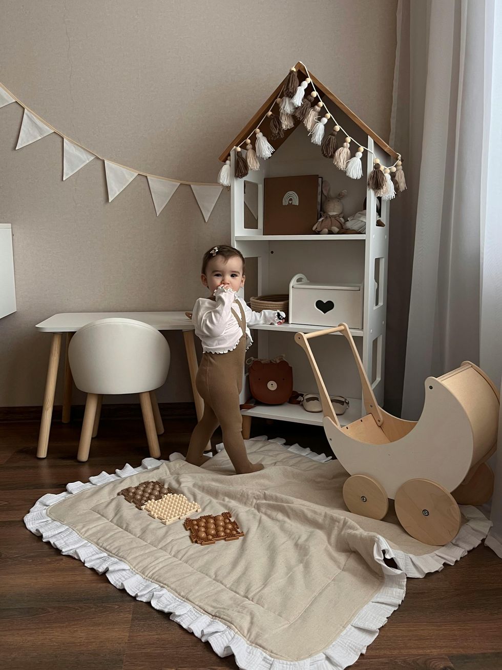 Toddler in cozy room with toys, tent, and decorative bunting.