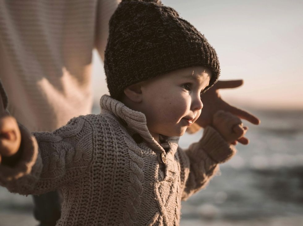Toddler in knit hat and sweater, exploring outdoors at sunset.