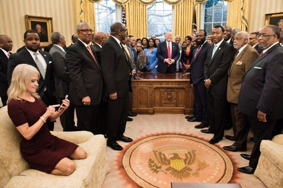TOPSHOT - Counselor to the President Kellyanne Conway (L) checks her phone after taking a photo as US President Donald Trump and leaders of historically black universities and colleges pose for a group photo in the Oval Office of the White House before a meeting with US Vice President Mike Pence February 27, 2017 in Washington, DC. / AFP / Brendan Smialowski (Photo credit should read BRENDAN SMIALOWSKI/AFP/Getty Images)