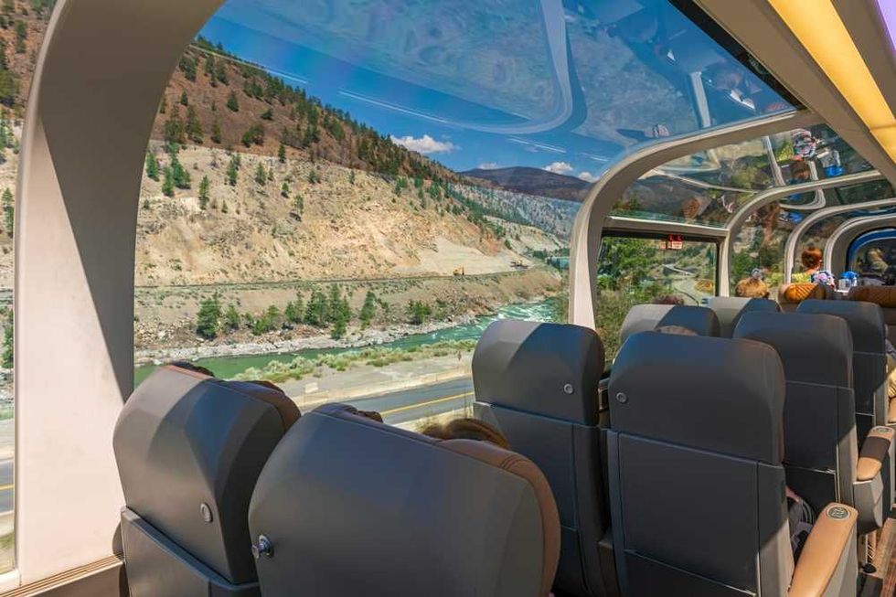 Train interior with large windows showing scenic mountain and river views.