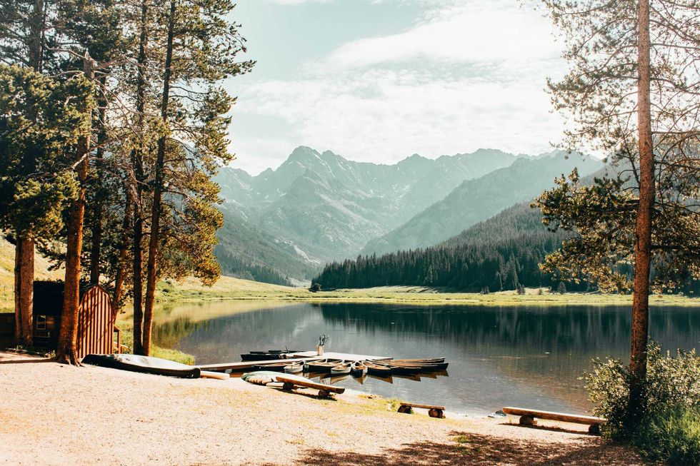 Tranquil lake with boats, surrounded by trees and mountains under a cloudy sky.