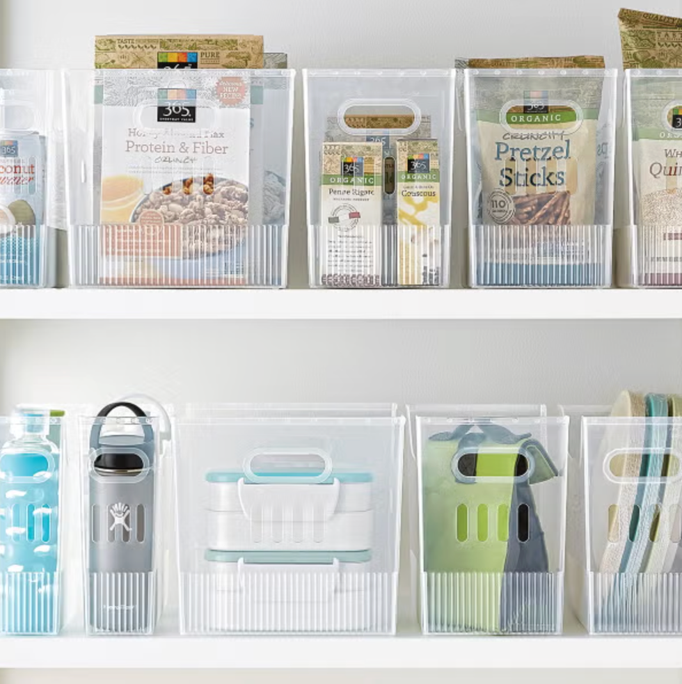 Transparent bins neatly organized on white shelves with various pantry items and bottles.