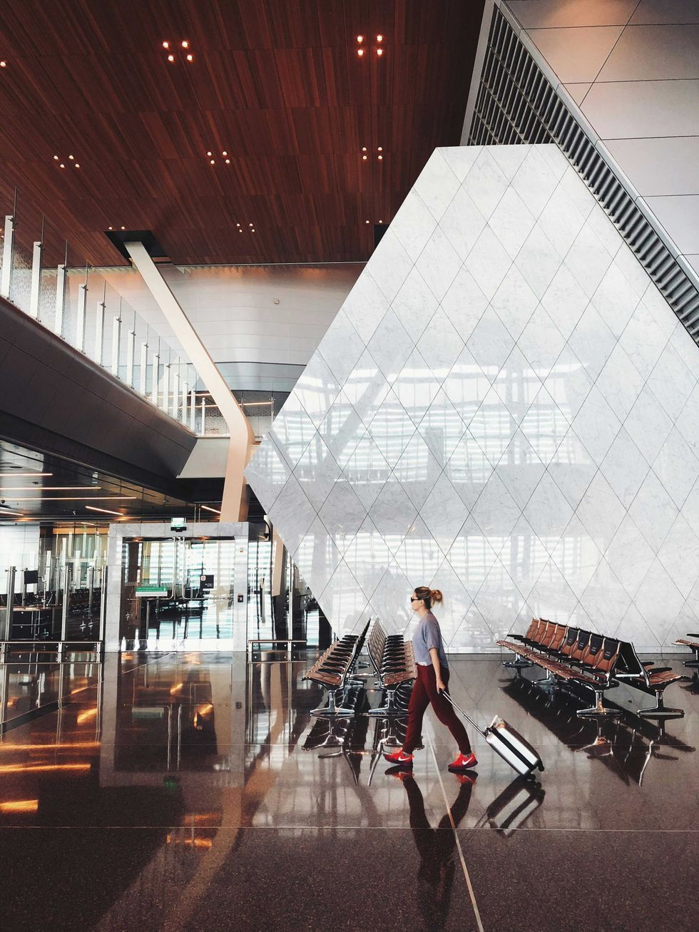 Traveler with suitcase walking through a modern, spacious airport terminal.