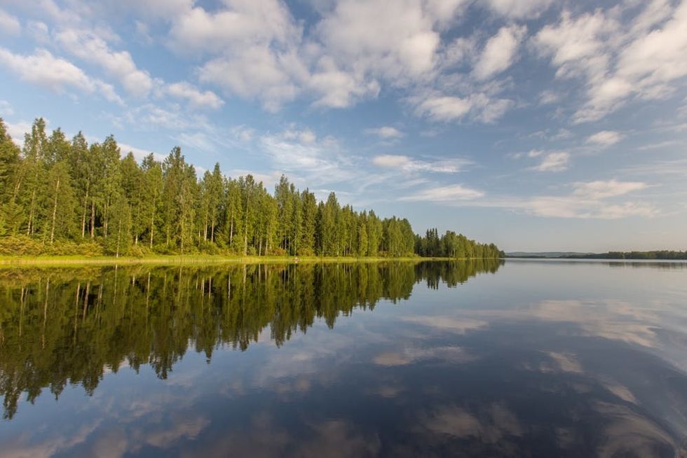 Trees, clouds, and blue sky reflect in the clear waters of a Finnish lake