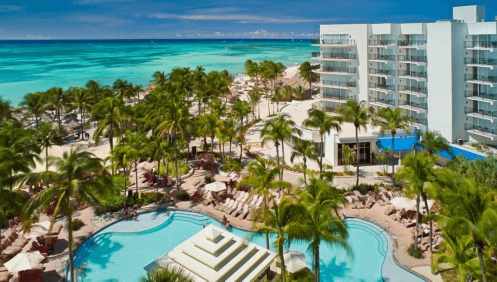 Tropical beach resort with pools, palm trees, and ocean view from a high vantage point.