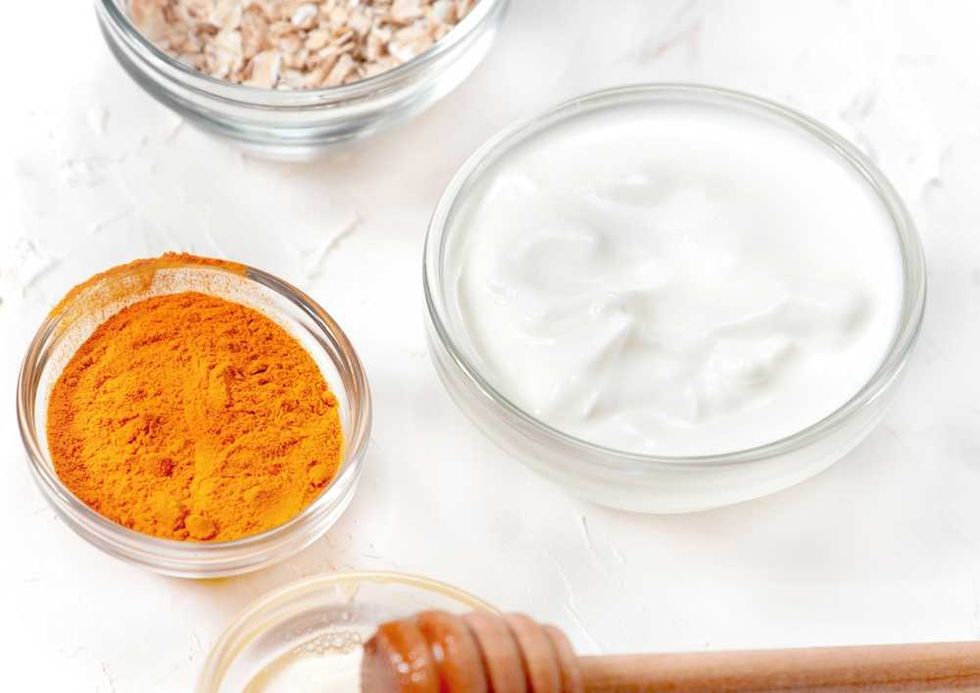Turmeric, yogurt, oats, and honey in bowls on a white background.