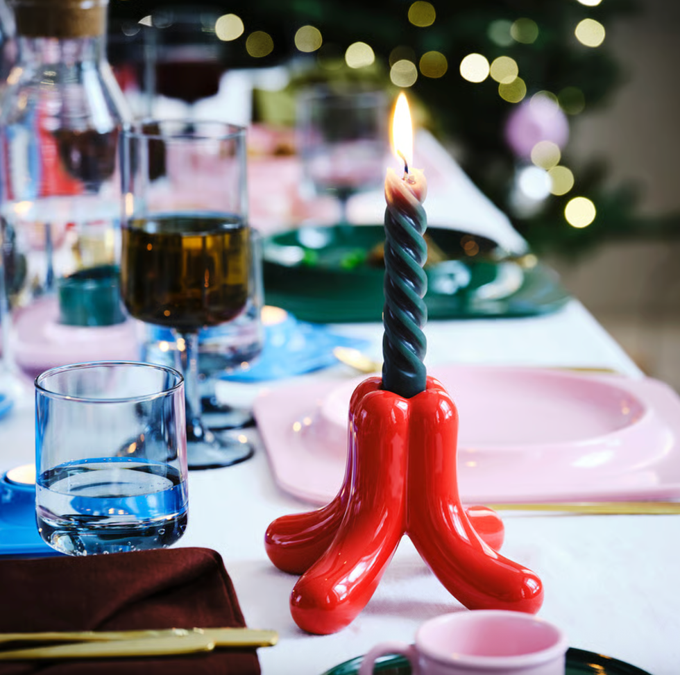 Twisted candle in a red holder on a festive dining table setup with glasses and plates.