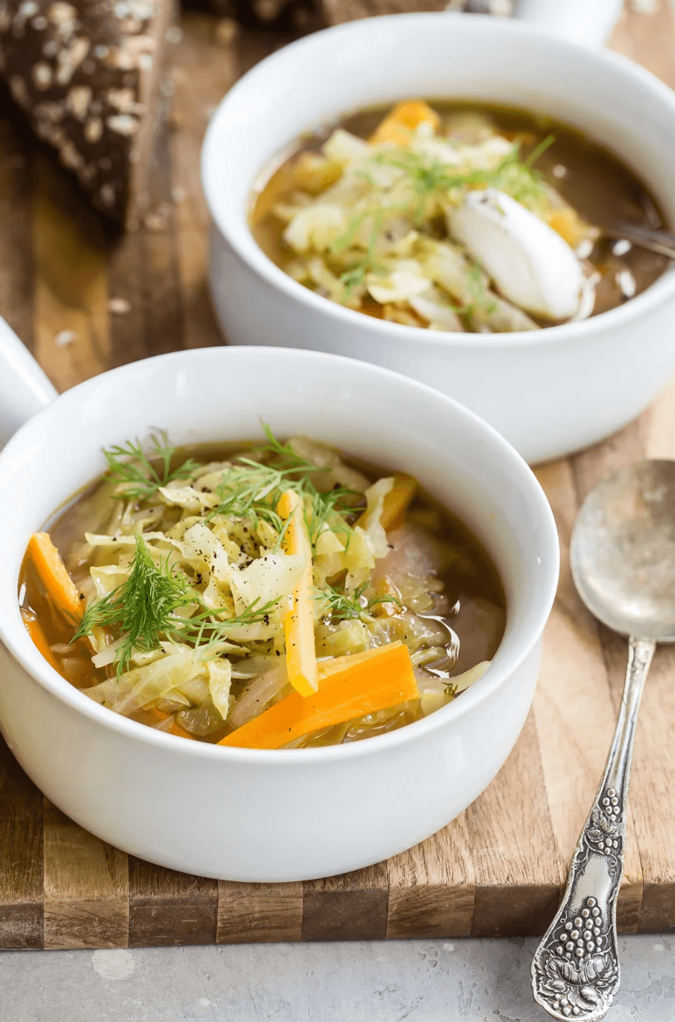 Two bowls of clear vegetable soup with herbs and a vintage spoon on the side.