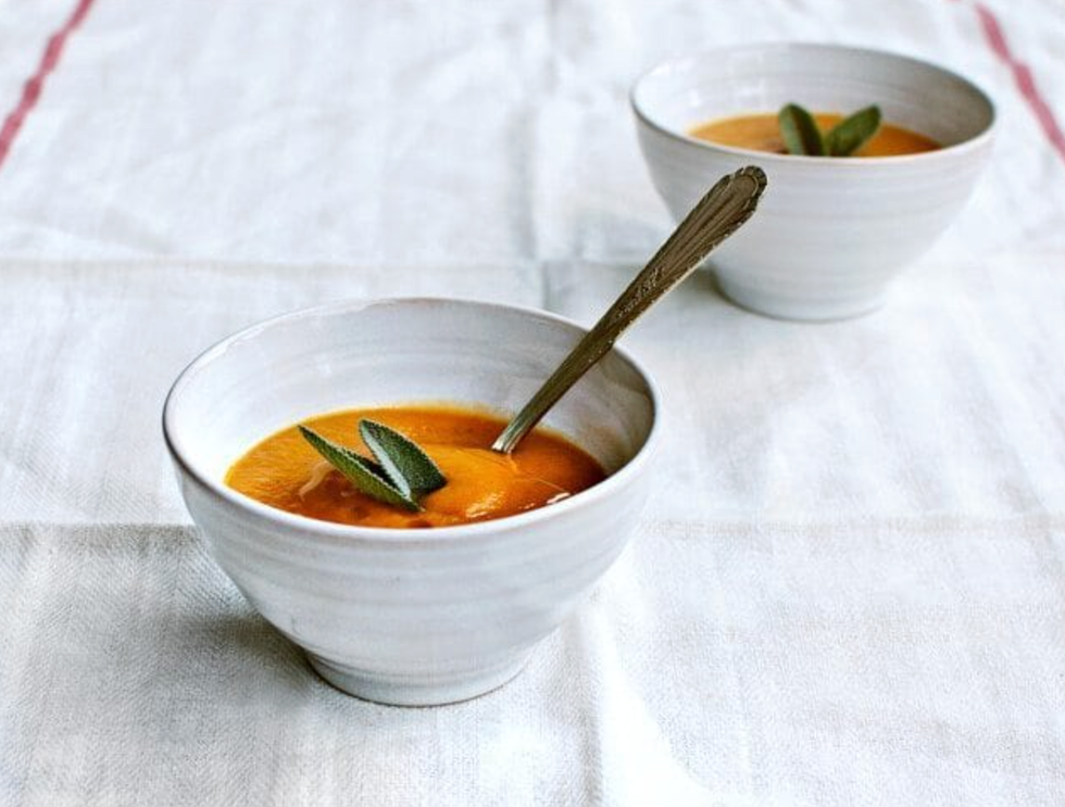 Two bowls of pumpkin soup with sage leaves on a white tablecloth.
