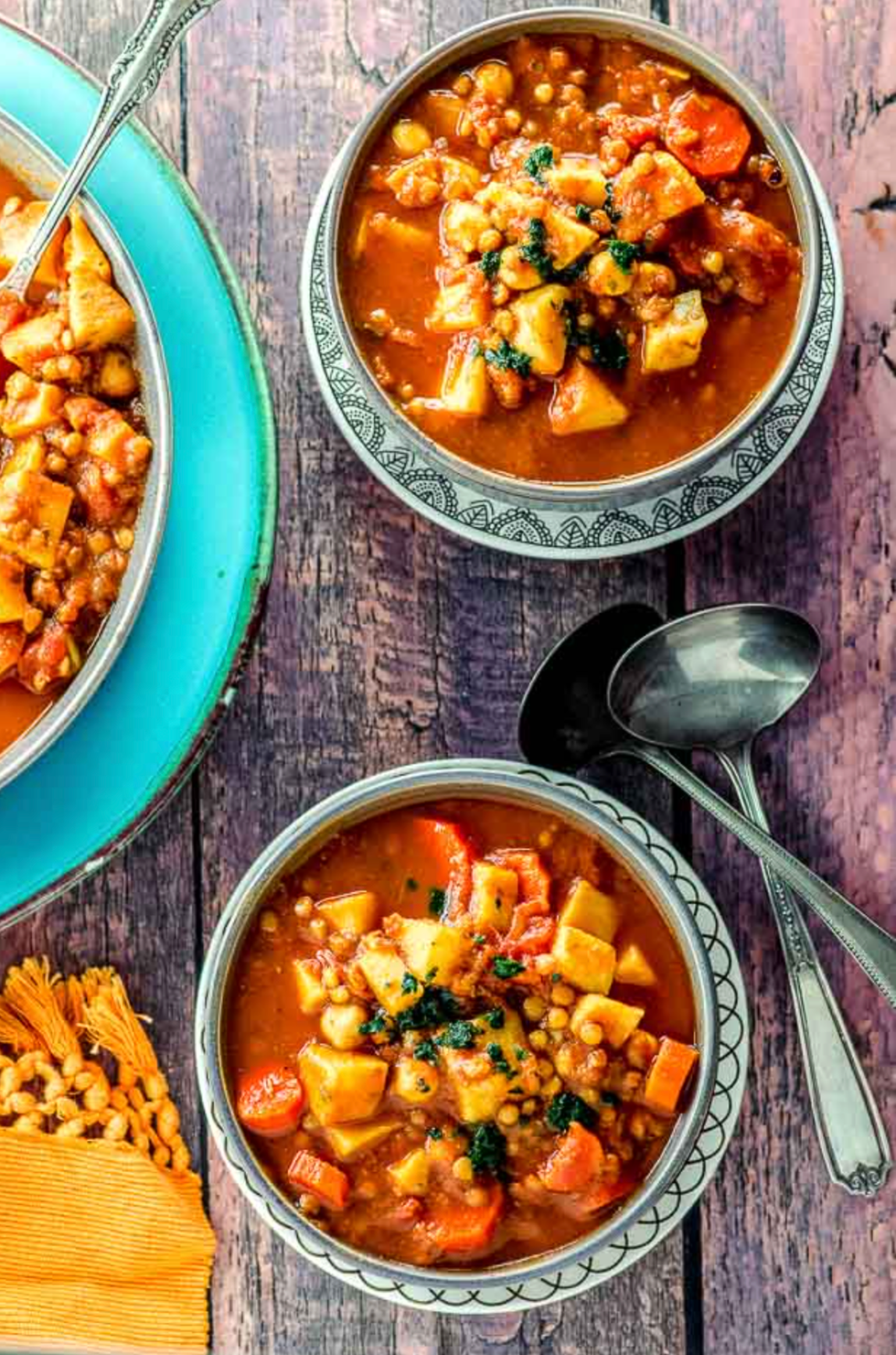 Two bowls of vegetable stew with spoons on a rustic wooden table.
