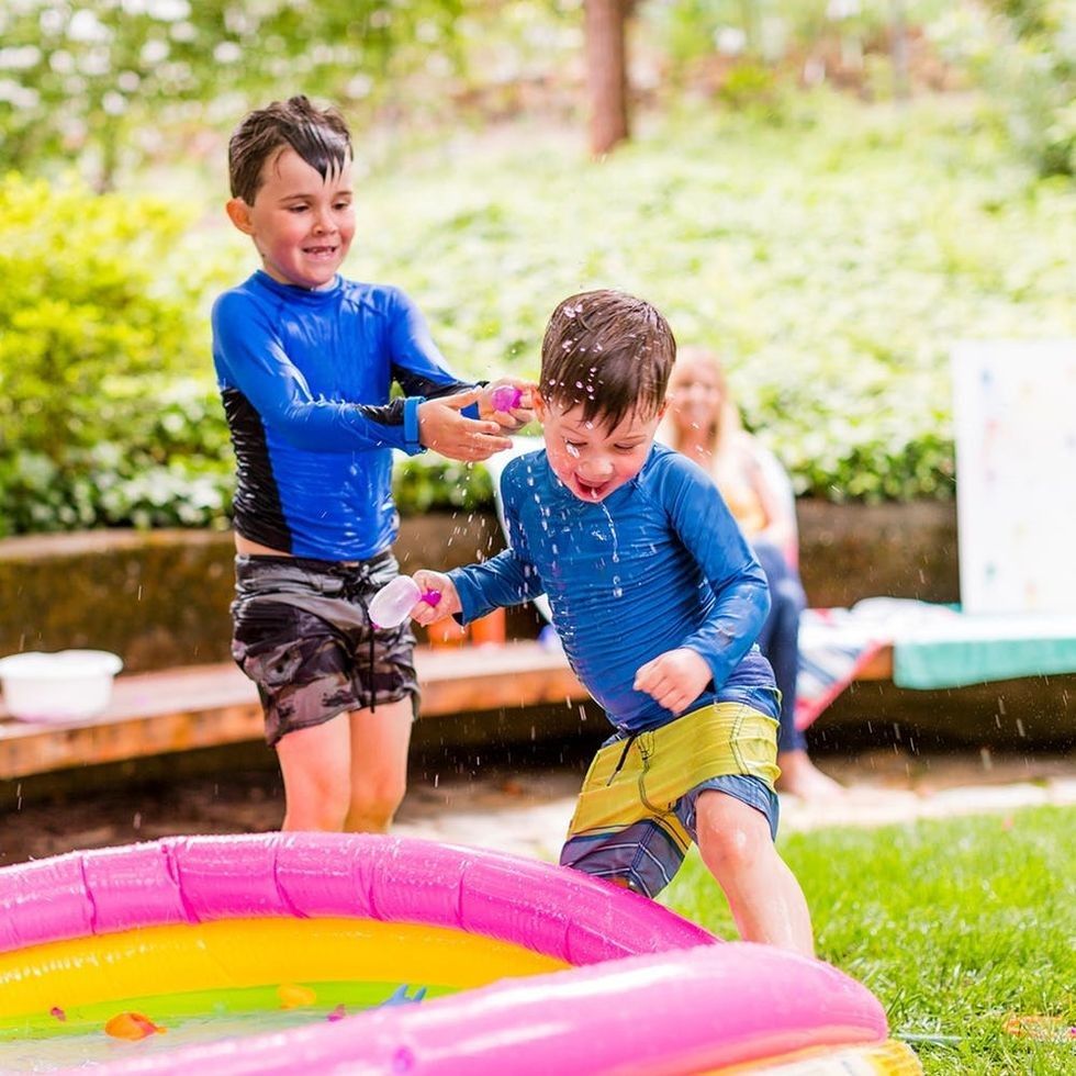 Two boys playing with water near a colorful inflatable pool in a garden.