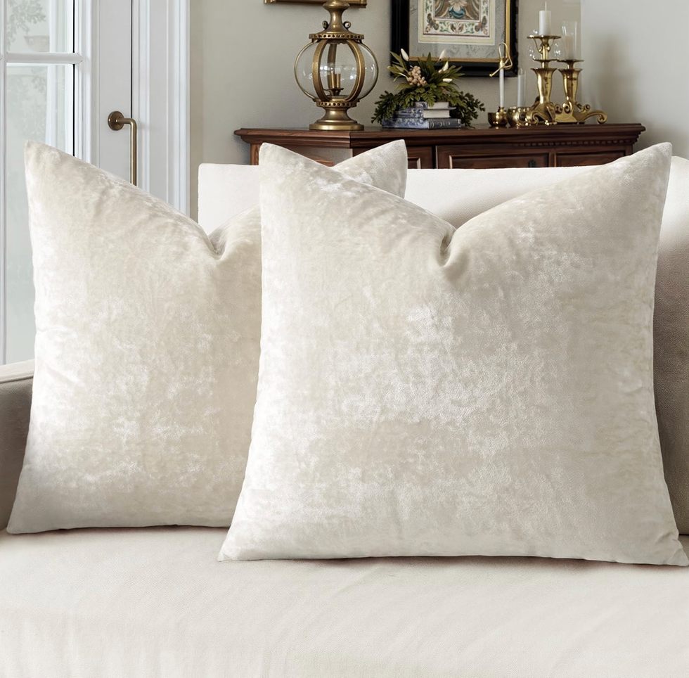 Two cream velvet pillows on a beige sofa in a cozy living room.
