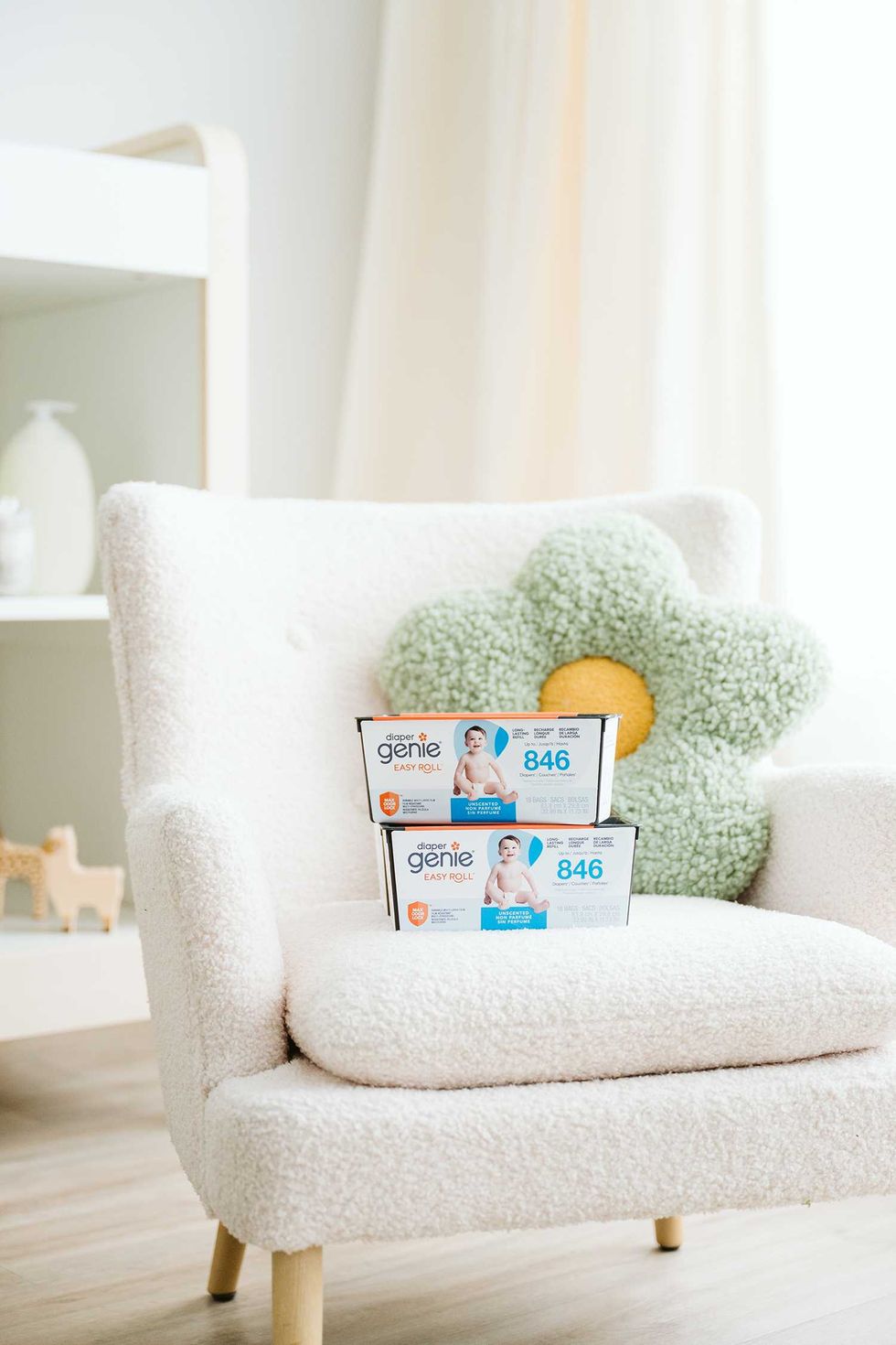 Two Diaper Genie boxes on a white chair with a flower cushion.