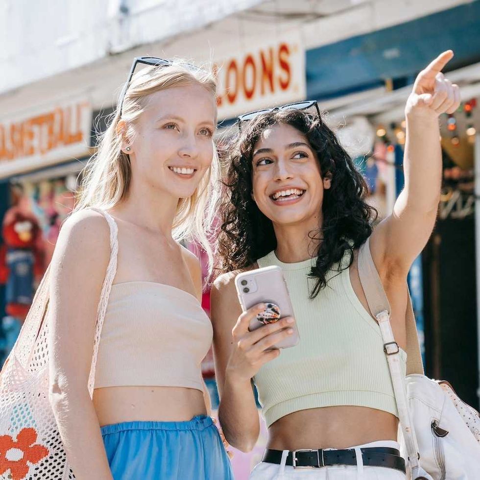 Two friends smiling and pointing while sightseeing and holding a smartphone.