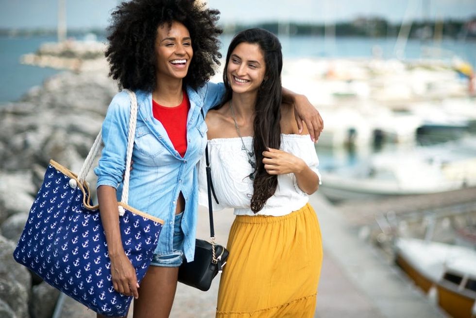 Two friends walk arm-in-arm down a pier at a marina