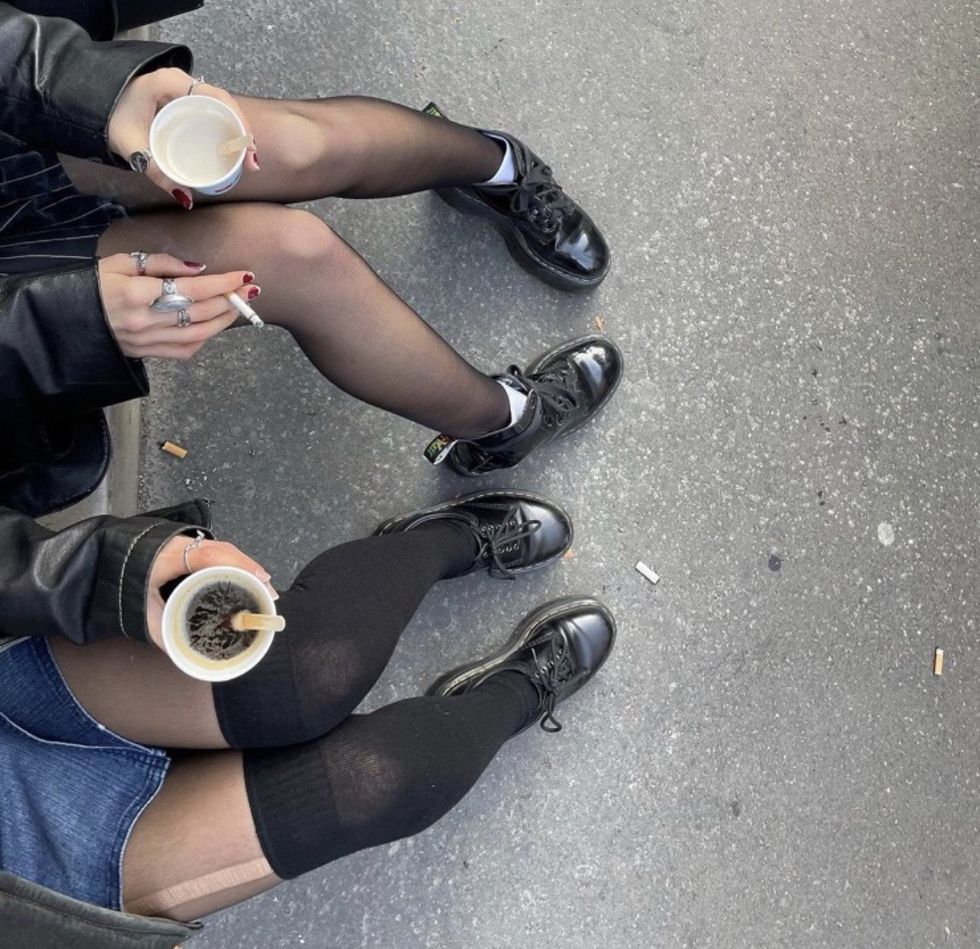two girls sitting on pavement with knee socks and coffee