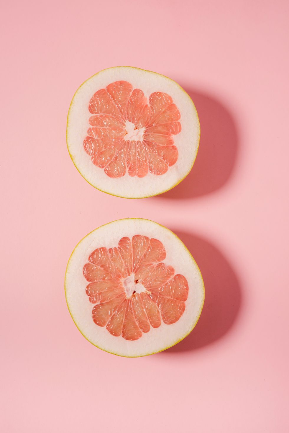 two Grapefruit slices against a pink background
