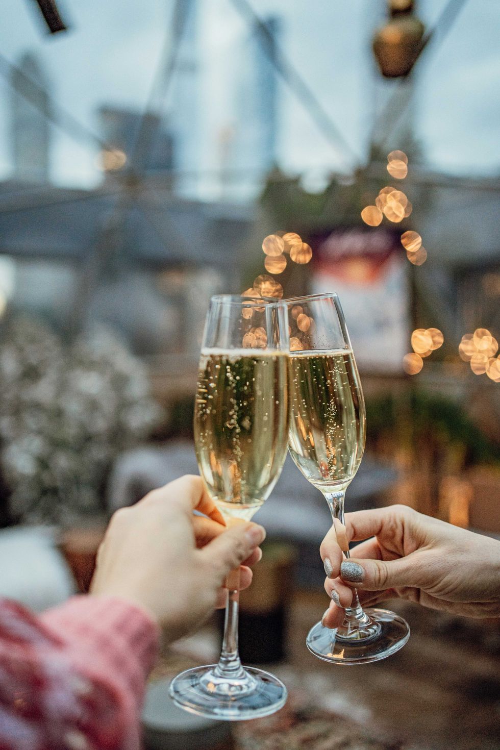 Two hands clinking champagne glasses against a bokeh-lit background.