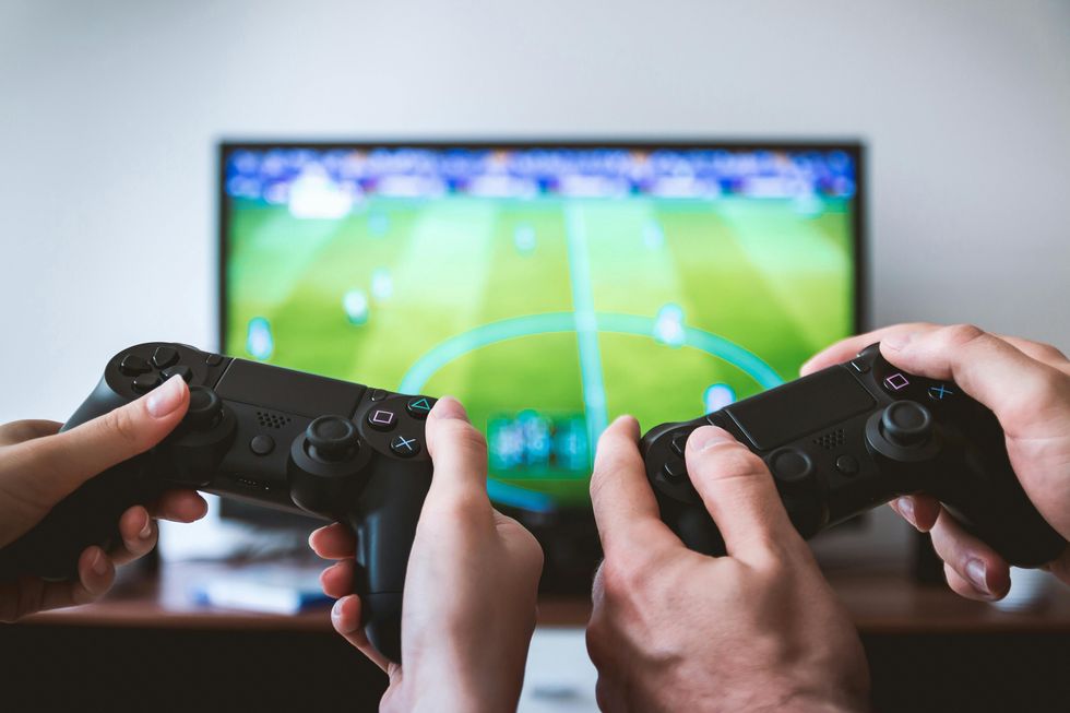 Two hands holding game controllers, playing soccer on a TV screen.