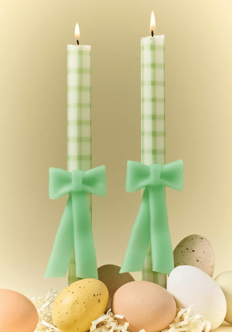 Two lit green plaid candles with bows, surrounded by colorful eggs.