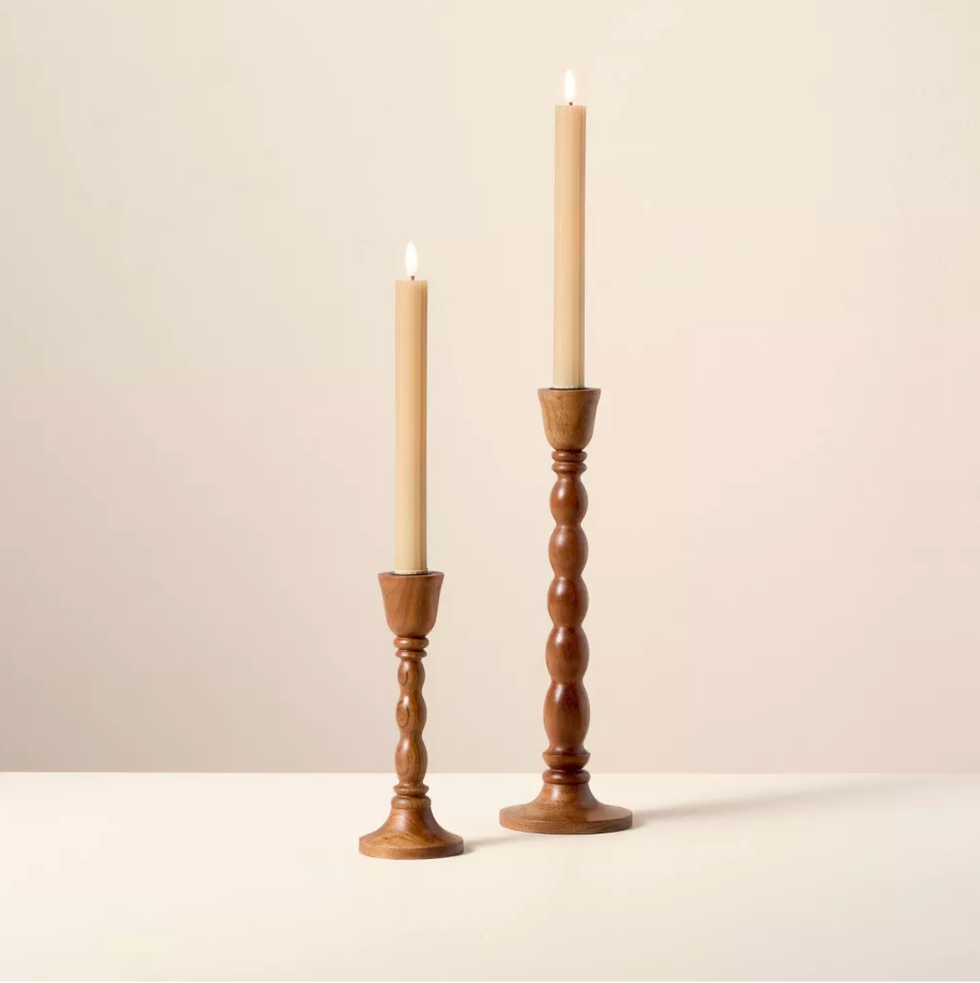 Two lit wooden candlesticks of different heights on a light surface.