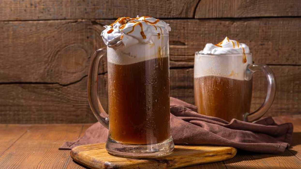 Two mugs of root beer float with whipped cream and caramel, on a wooden board.