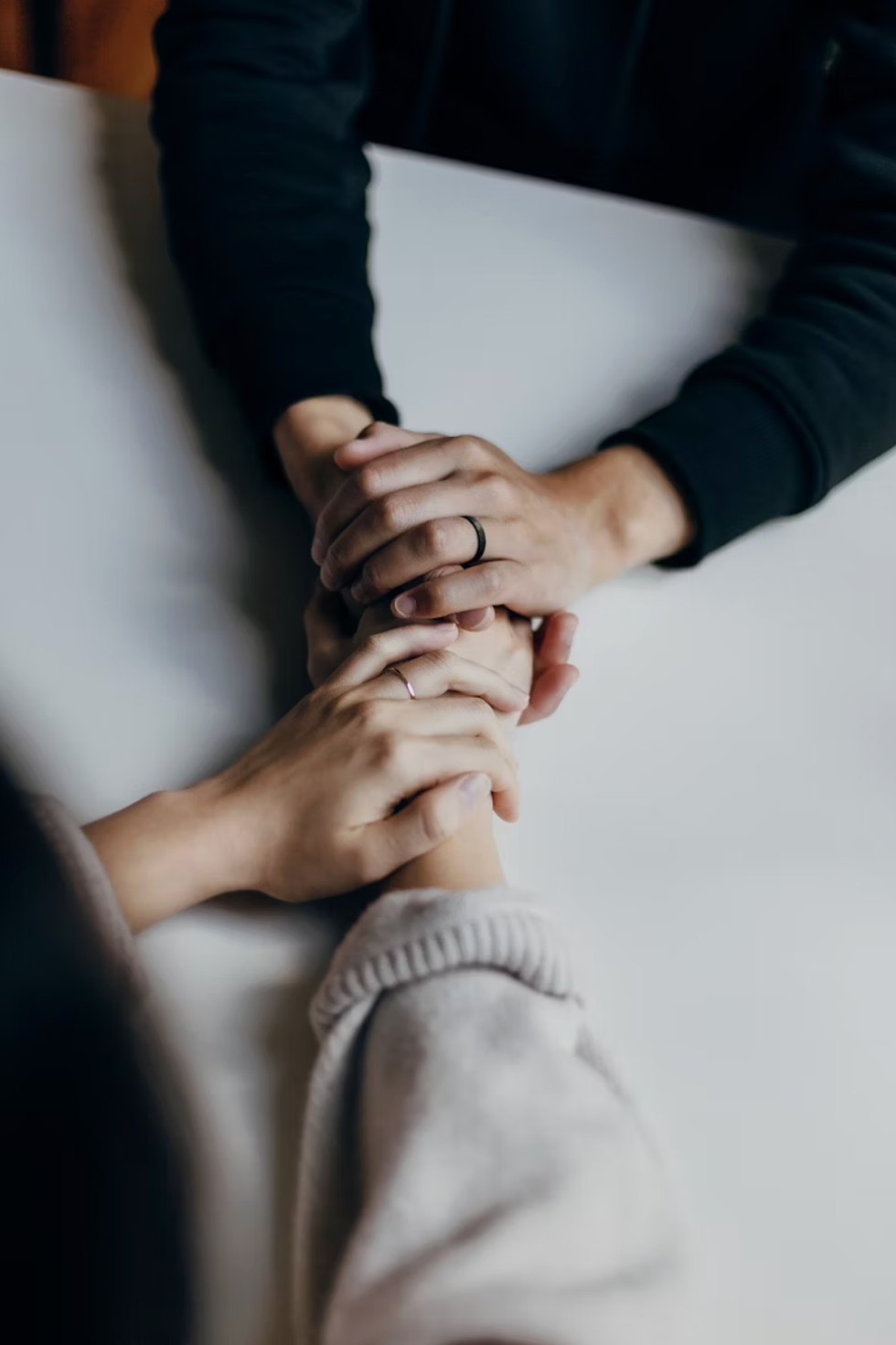 Two pairs of hands clasped together on a white table, showing support and connection.