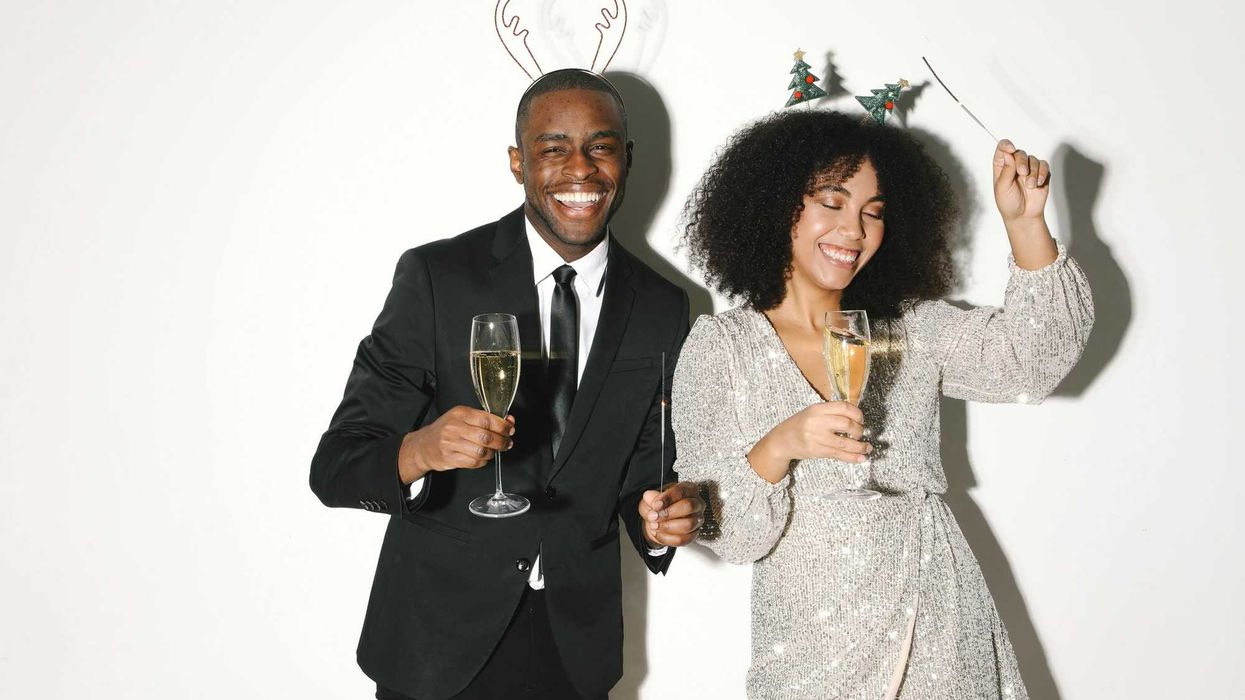 Two people celebrating, wearing festive headbands, holding champagne glasses, smiling.