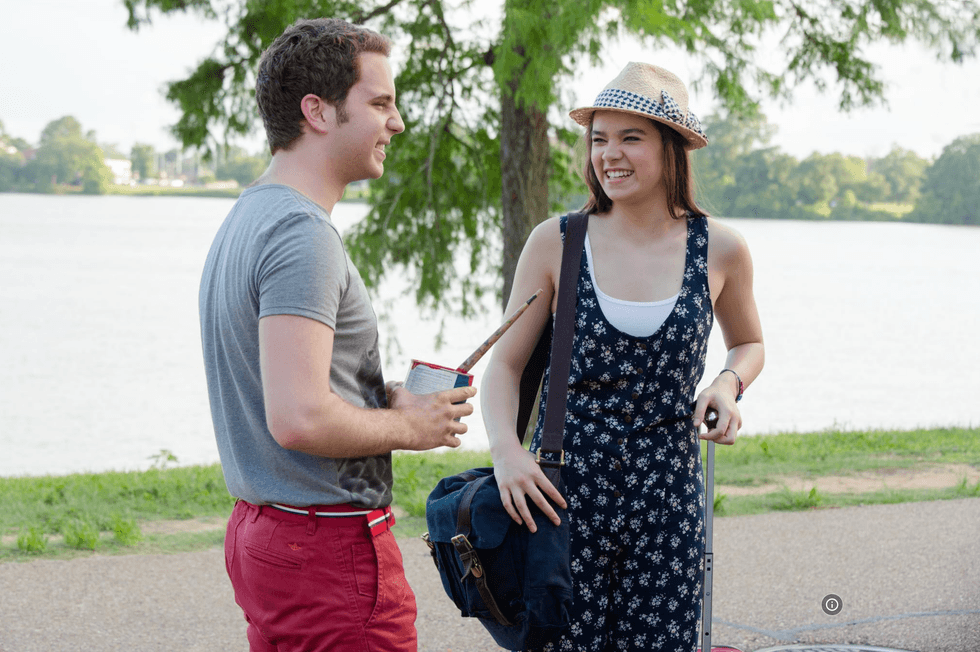 Two people chatting happily by a lakeside, one holding paint supplies.