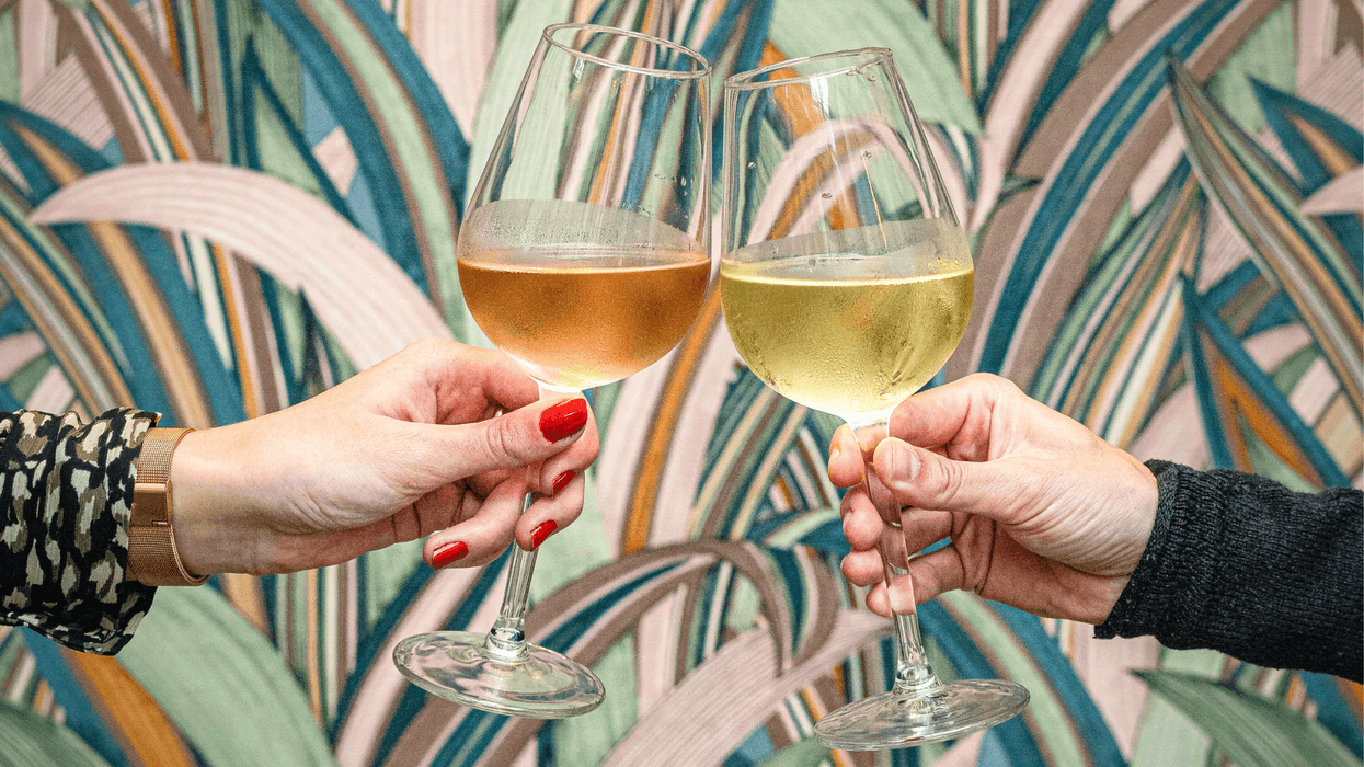 Two people clinking white wine glasses against a colorful abstract wallpaper.
