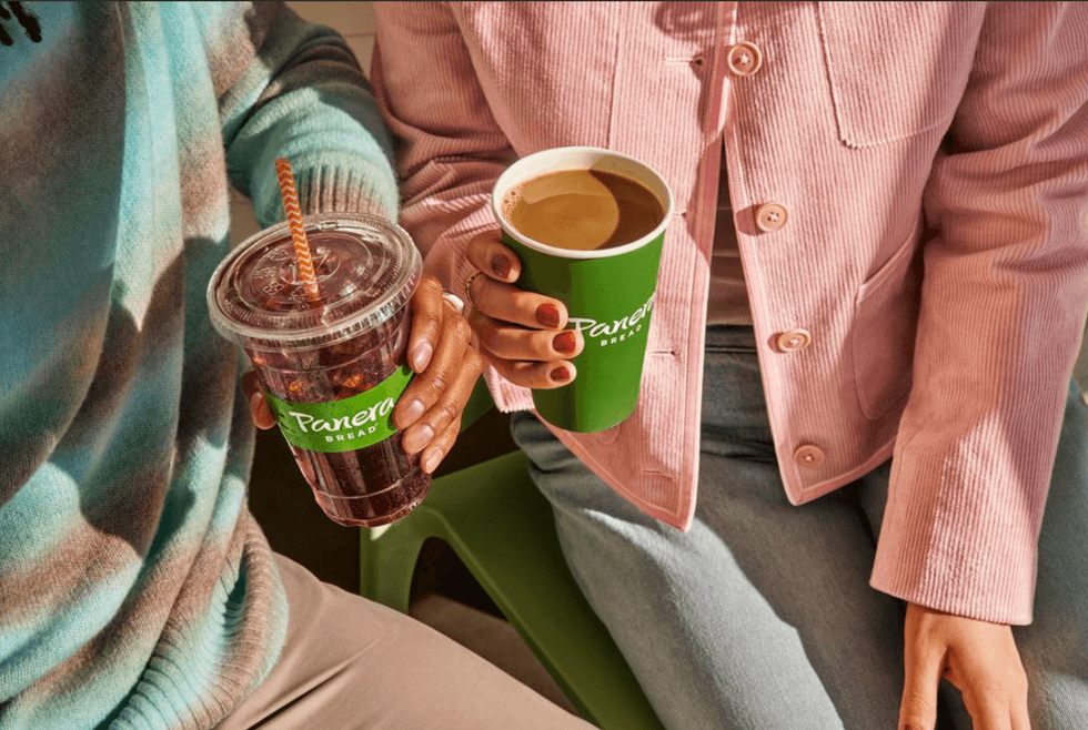 Two people holding Panera Bread drinks, one iced and one hot, sitting side by side.