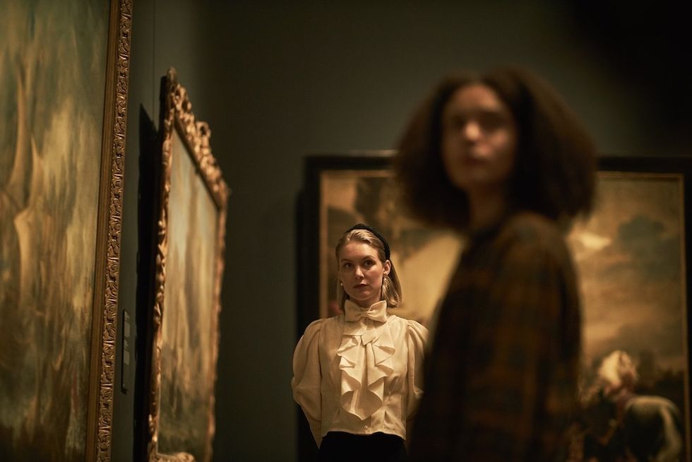 Two people in a dimly lit gallery, with paintings on the walls.