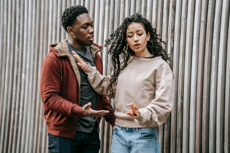 Two people in a discussion by a wooden fence.