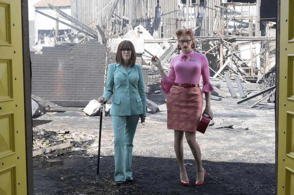 Two people in colorful outfits stand amid a charred, abandoned building site.