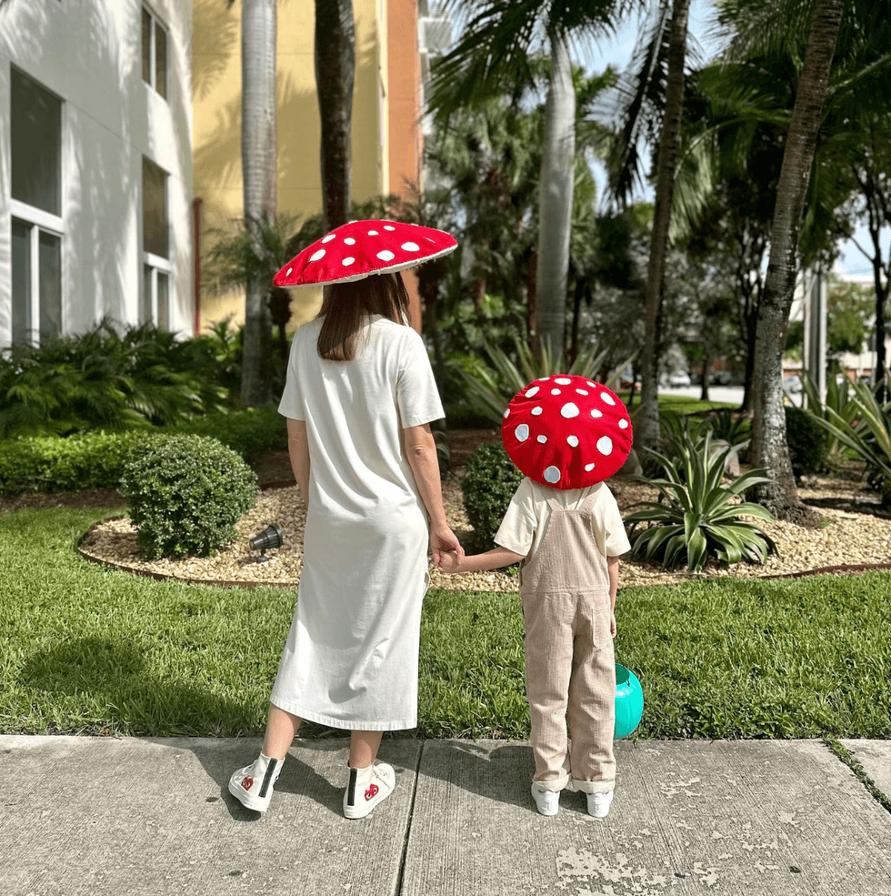 Two people in mushroom hats holding hands, standing on a sidewalk.
